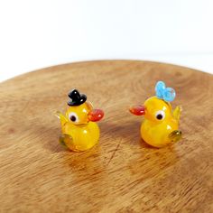 two yellow rubber ducks sitting on top of a wooden table with one wearing a black hat