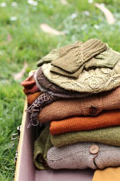 an open suitcase filled with sweaters and scarves on the green grass in a park