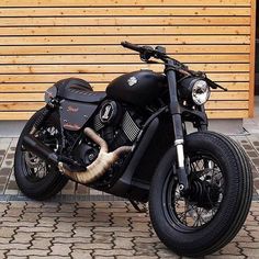 a black motorcycle parked in front of a wooden wall with an animal's tail sticking out of it