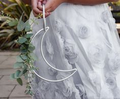 a woman in a white dress holding a metal hoop with flowers and greenery on it