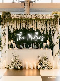 a table with white flowers and candles under a neon sign that says the millies