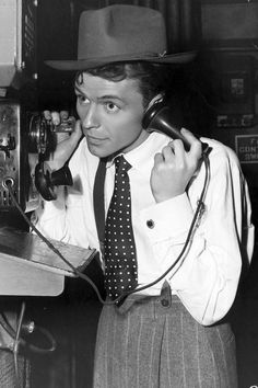 a man in a suit and tie talking on a telephone while wearing a fedora