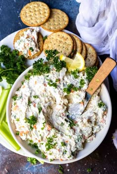 a white bowl filled with food next to crackers and celery on a table