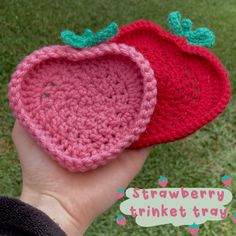 two crocheted strawberries are in the palm of someone's hand on grass