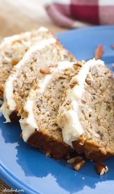 two slices of banana bread with white frosting on a blue plate next to some pecans