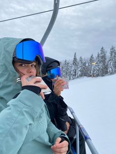 a woman sitting on top of a snow covered ski slope while holding onto a drink