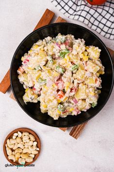 a black bowl filled with pasta salad next to a wooden spoon and tomatoes on the side