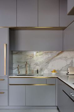 a kitchen with grey cabinets and marble counter tops, gold trimmings on the backsplash