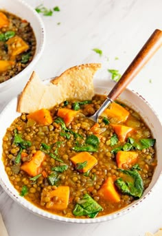 two bowls filled with lentils and spinach on top of a white table next to crackers