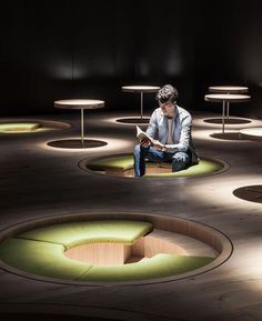 a man sitting on the ground in front of some tables with lights around him and reading a book