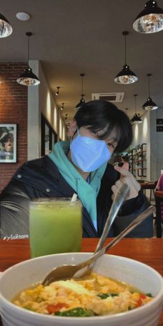 a woman wearing a face mask while eating food at a restaurant with a green smoothie in front of her