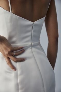 a woman in a white dress with her hand on the back of her dress,