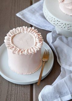 a pink frosted cake sitting on top of a white plate next to a knife and fork