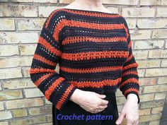 a woman standing in front of a brick wall wearing an orange and black crochet sweater