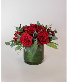 a vase filled with red roses and greenery