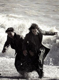 black and white photograph of two people playing in the water at the beach with waves crashing behind them