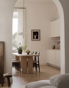 a dining room table with chairs and a potted plant in the center is seen through an archway