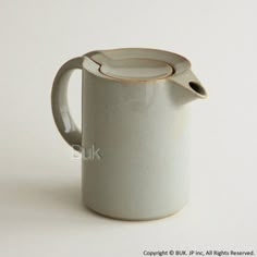 a white coffee pot with a brown handle on a white tableclothed surface, in front of a plain background