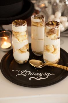 three desserts sitting on top of a black plate next to two gold spoons