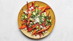 a yellow plate topped with carrots and broccoli covered in feta cheese