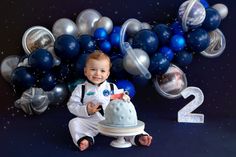 a baby boy sitting in front of a cake with the number two on it and balloons behind him