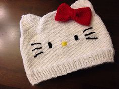 a knitted hello kitty hat with a red bow on the top, sitting on a table