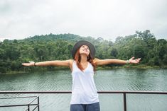 a woman with her arms outstretched in front of a body of water and trees on the other side