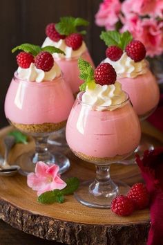 three desserts with raspberries and whipped cream are on a wooden platter