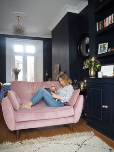 a woman sitting on top of a pink couch in a living room next to a window