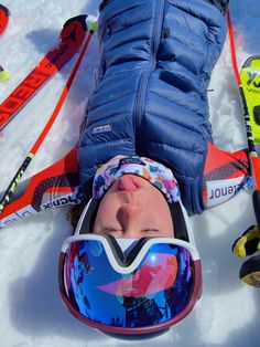 a young child laying on the snow with skis and goggles around his neck