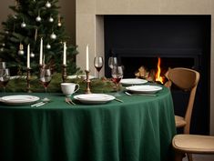 a table set for christmas with wine glasses, plates and candles in front of a fireplace