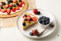 a piece of fruit pizza on a plate next to a bowl of berries