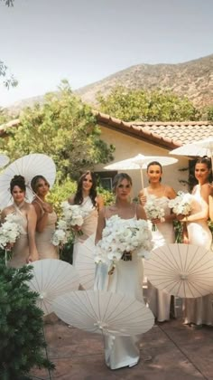 a group of bridesmaids holding umbrellas and flowers in front of a house