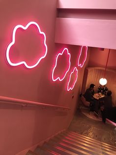 people are sitting at a table in a pink room with neon clouds on the wall