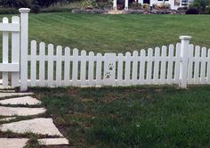 a white picket fence sitting in the middle of a grass covered field next to a house