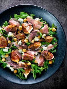 a black plate filled with salad and meats on top of it's sides