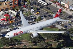 an airplane is flying over a city with cars and buildings in the background, as seen from above