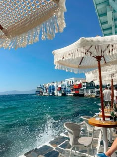 people sitting at tables under umbrellas near the ocean