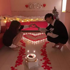 two people kneeling down in front of a heart - shaped cake with candles on it