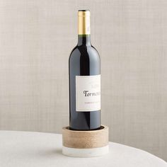 a bottle of red wine sitting on top of a white table next to a wall