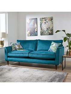 a living room scene with focus on the blue couch and rug, there is a large window in the background