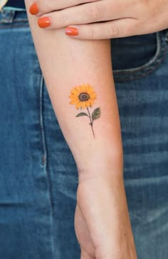 a woman's arm with a small sunflower tattoo on the left side of her arm