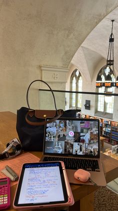 an open laptop computer sitting on top of a wooden desk next to a purse and cell phone