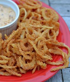 a red plate topped with onion rings next to a bowl of dip