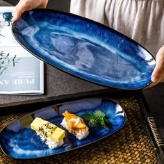 a person holding a blue plate with food on it next to a book and cup