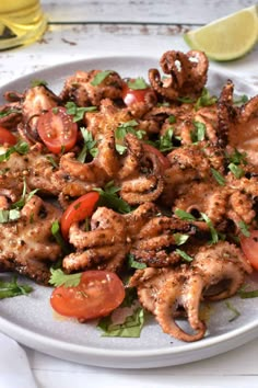 a white plate topped with grilled octopus next to sliced tomatoes and cilantro