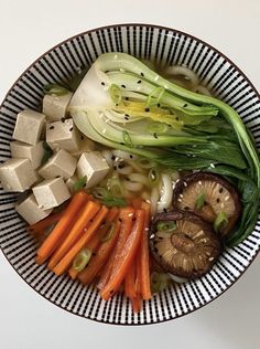 a bowl filled with vegetables and tofu on top of a white countertop next to sliced mushrooms