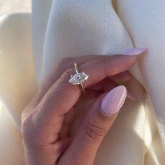 a woman's hand holding an engagement ring with a diamond in it on top of a white cloth