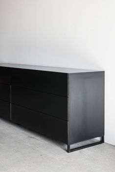 a large black dresser sitting on top of a floor next to a white wall in an empty room