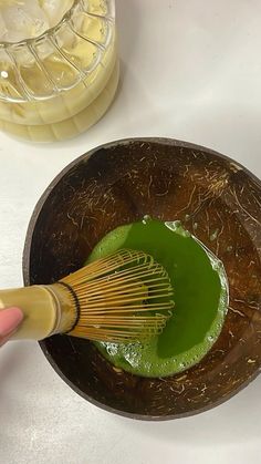 someone is whisking green liquid in a wooden bowl